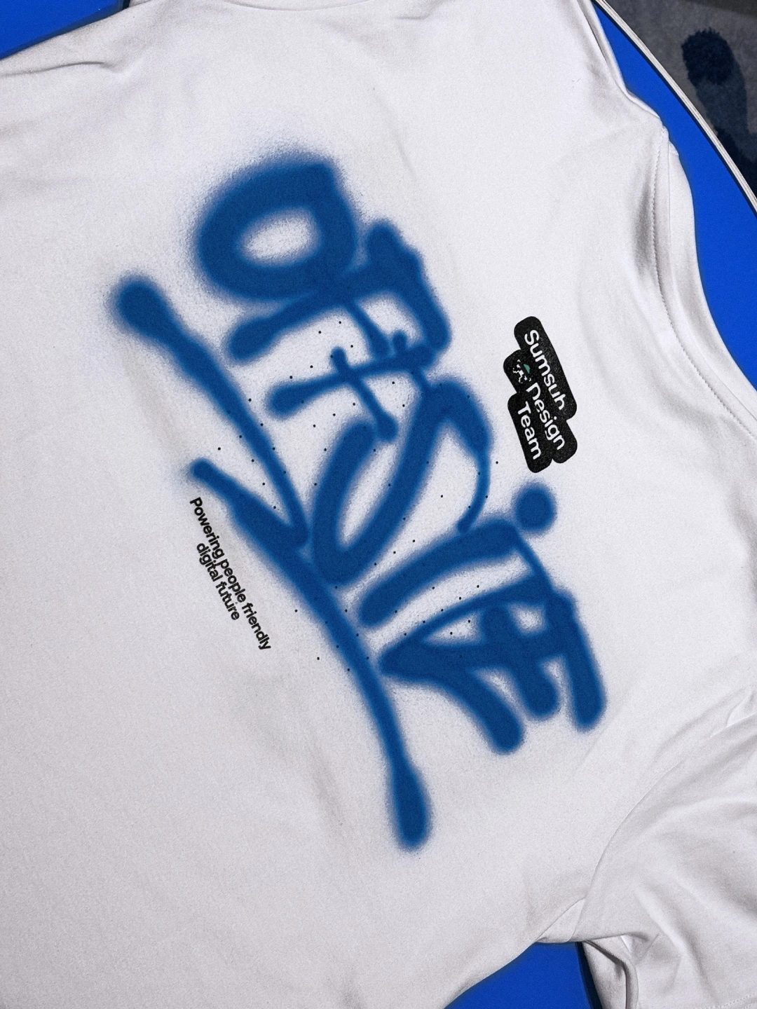 White T-shirt with hand-sprayed blue graffiti reading "Offsite" and a small black patch