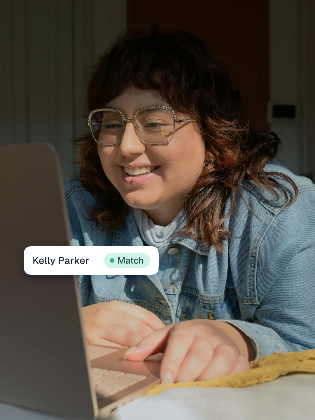 Smiling woman with glasses at a laptop, with a "Kelly Parker—Match" verification tag